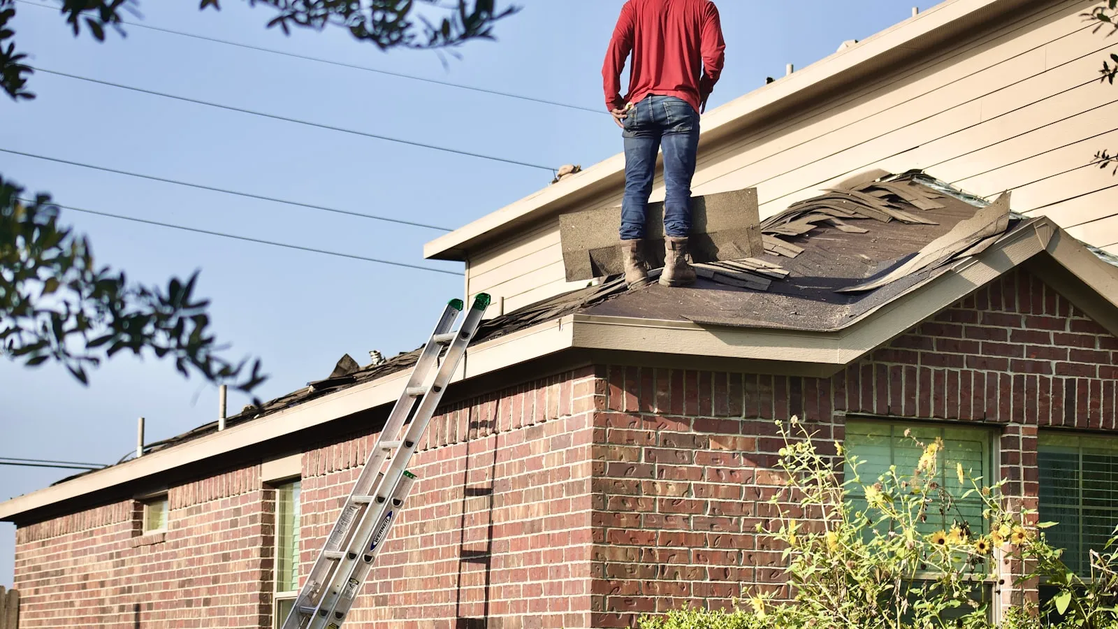 Inspector standing on the roof of a brick home beside a ladder