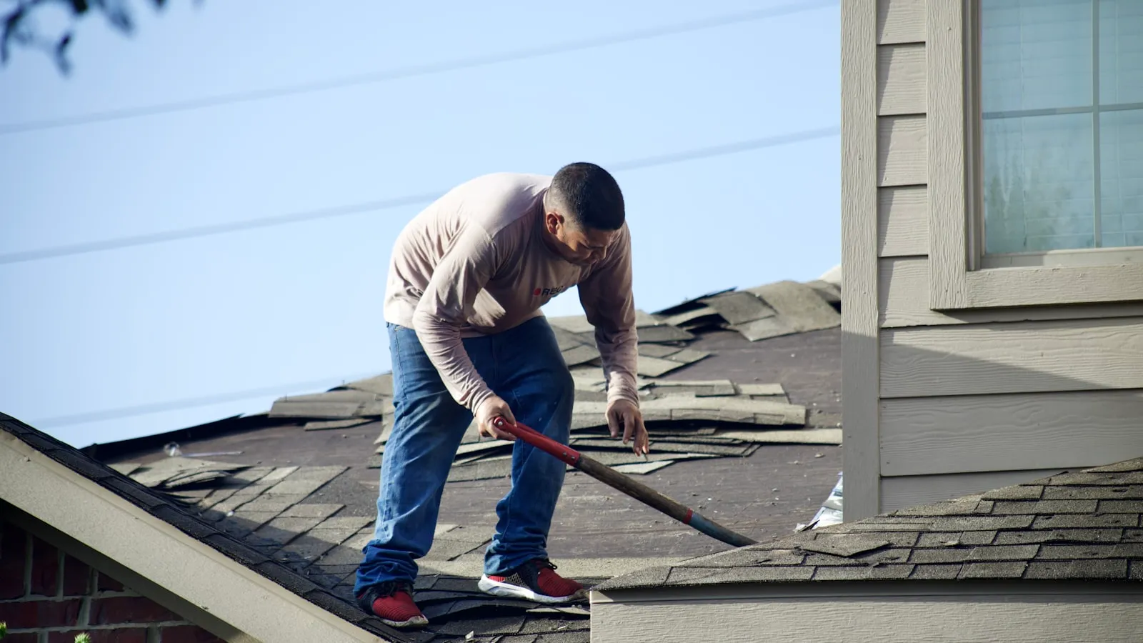 Roofer repairing shingles beside a dormer window on a residential roof